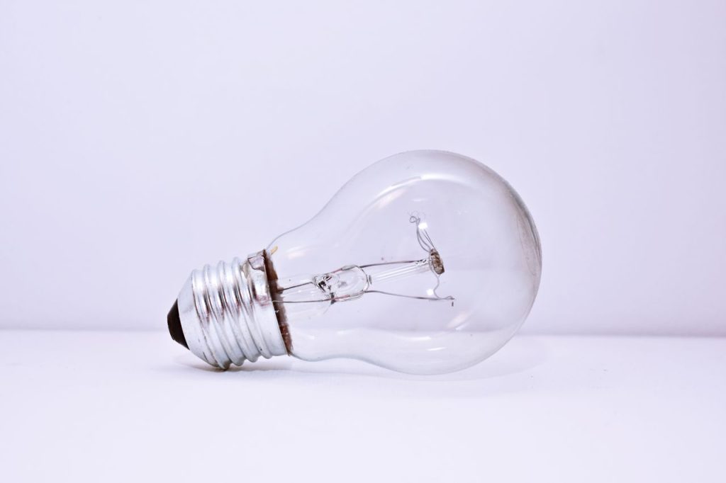 A clear incandescent light bulb lying on a simple white background, showcasing minimalism.