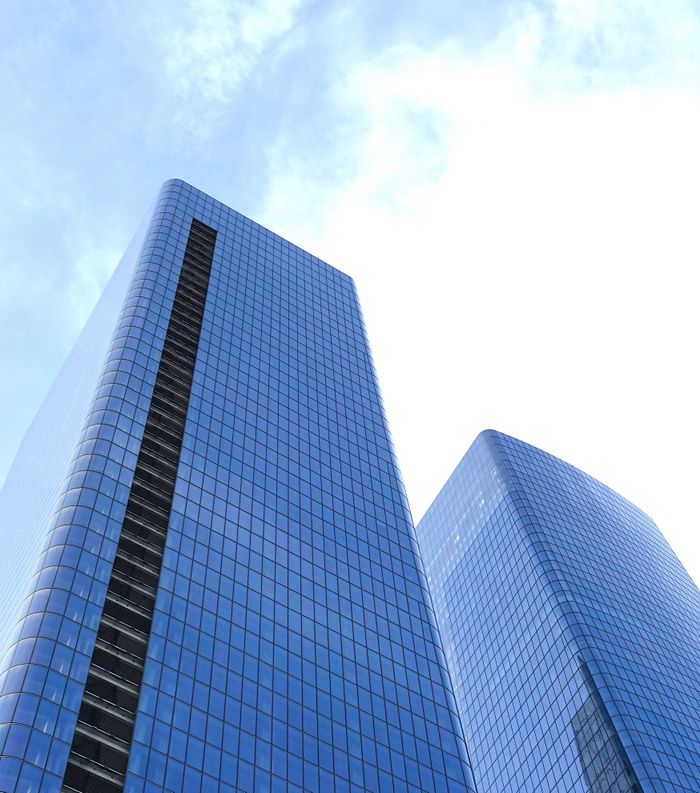 Low angle view of tall glass skyscrapers in New York City against a bright blue sky.